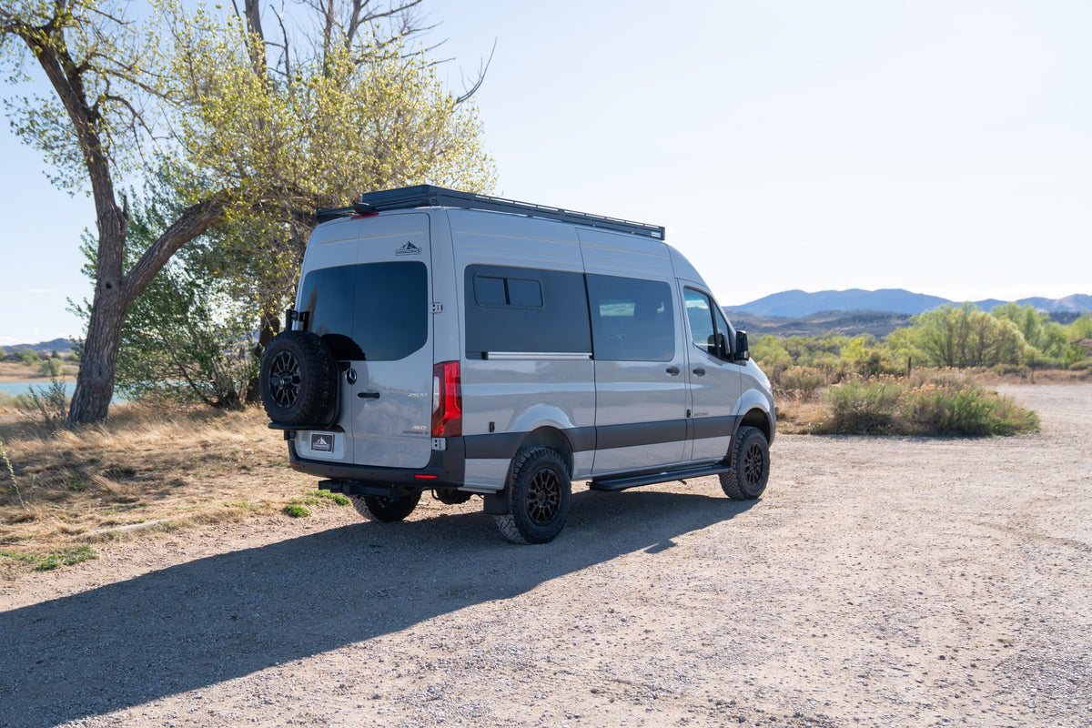 Light grey Mercedes-Benz Sprinter camper van (RV rental) parked on a gravel road, with a lake and mountains behind. — photo 2