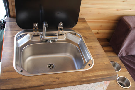 Compact RV rental kitchen features a stainless steel sink with a foldable faucet and wood countertop.