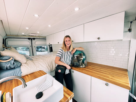 Happy woman & cat in a cozy, modern RV rental, featuring a bed, kitchen, and pet-friendly space.