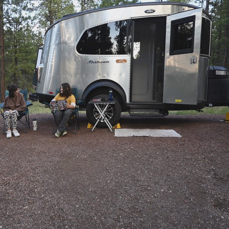 Two people lounge by their Airstream RV rental, embracing outdoor travel. A perfect setup for a relaxing camping trip.