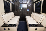 Inside a luxurious RV rental: cream quilted benches, dark wood-paneled walls, entertainment screen, and amenities.