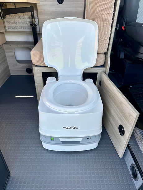 This rv rental shows a clean portable toilet (Porta Potti 345) inside a camper van, ideal for travel.