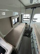 Efficient RV rental interior showcasing a comfortable bench bed, overhead storage, and accessible rear doors for camper van travels.