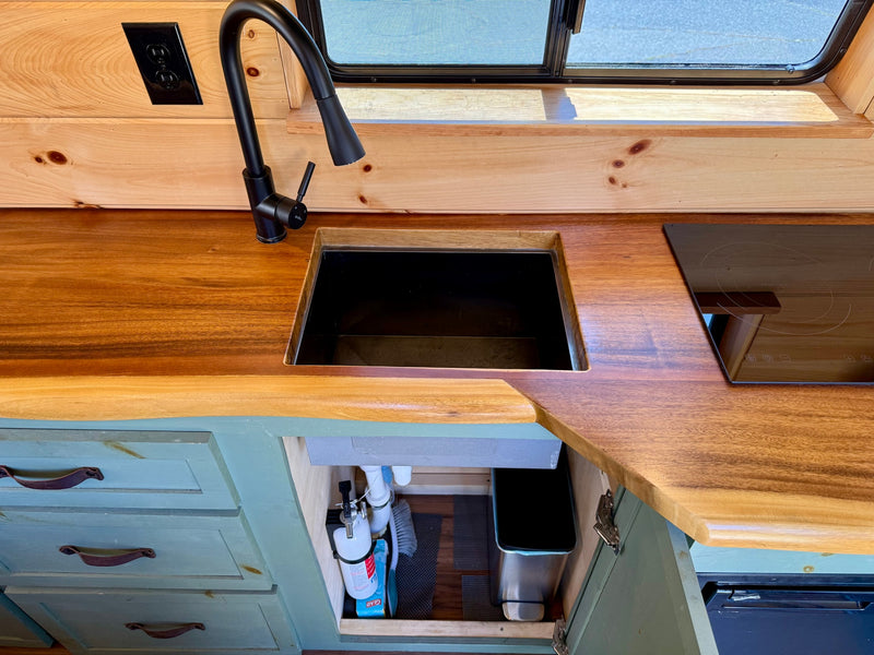 Modern RV rental kitchen with wood countertop, black sink, pull-down faucet, induction cooktop, and under-cabinet storage. — photo 12
