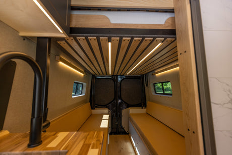 Inside a custom **camper van**: illuminated wooden ceiling, cozy benches, and kitchen. Perfect for your **RV rental** trip.