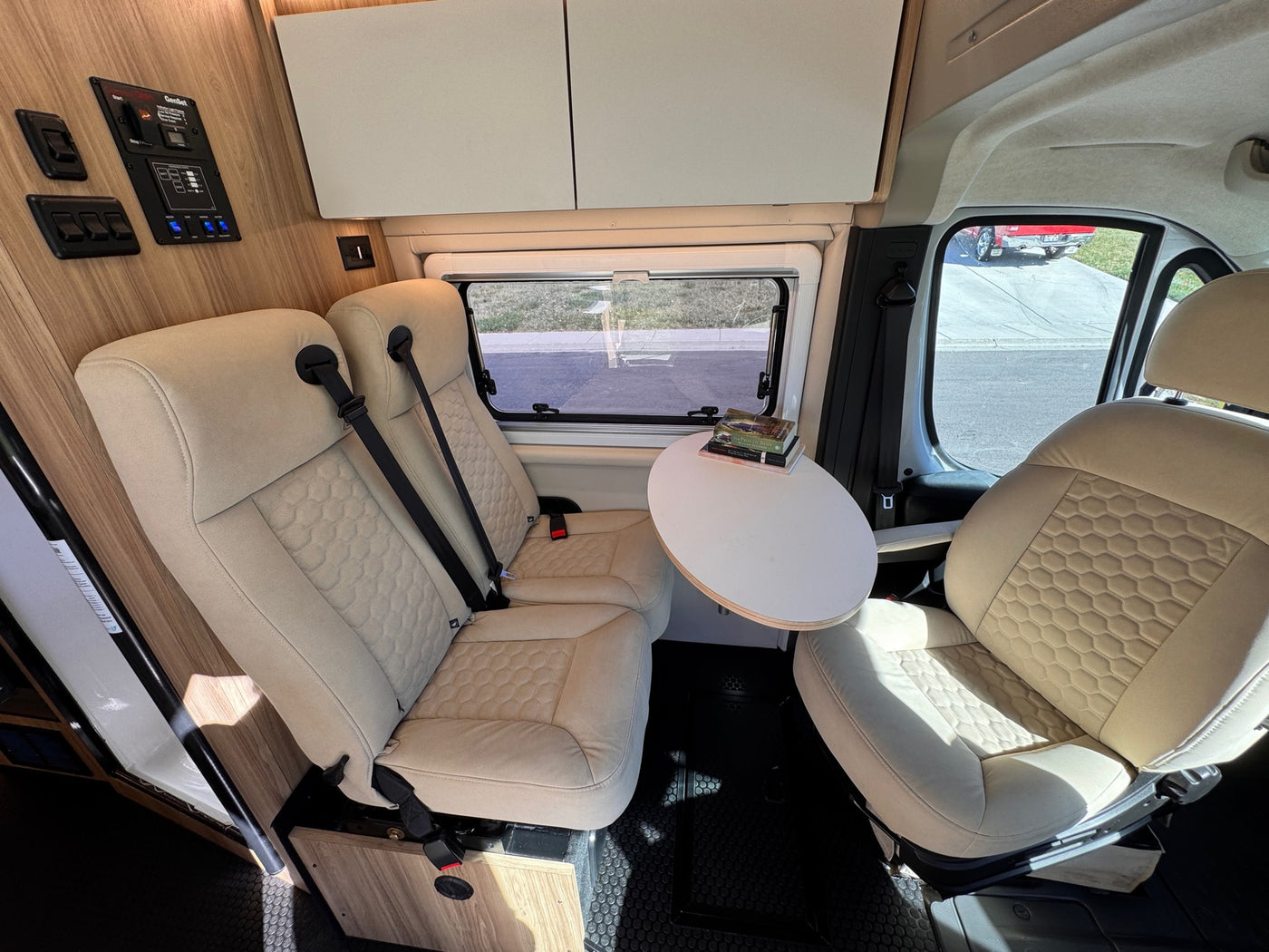 Modern RV rental interior: beige passenger seats, a small dining table, and a control panel for comfortable travel. — photo 10