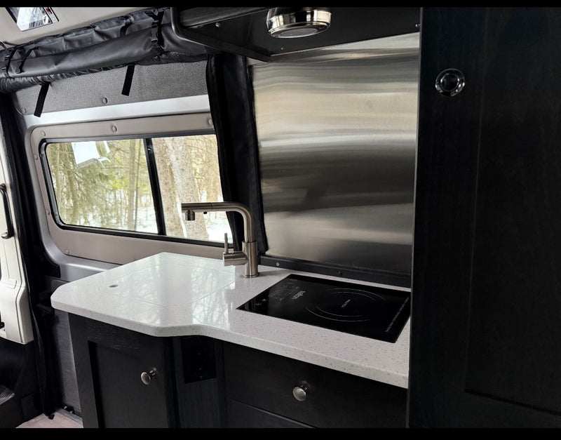 Modern RV rental kitchen with white speckled countertop, induction cooktop, and faucet, featuring a snowy view. — photo 10