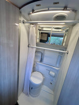Inside an RV rental: a compact wet bath featuring a toilet, shower, and mirror, designed for travel convenience.