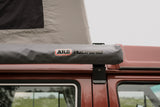 Reddish pop-top camper with ARB Touring awning.