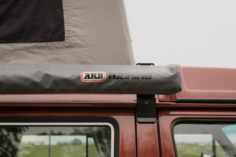 Reddish pop-top camper with ARB Touring awning.