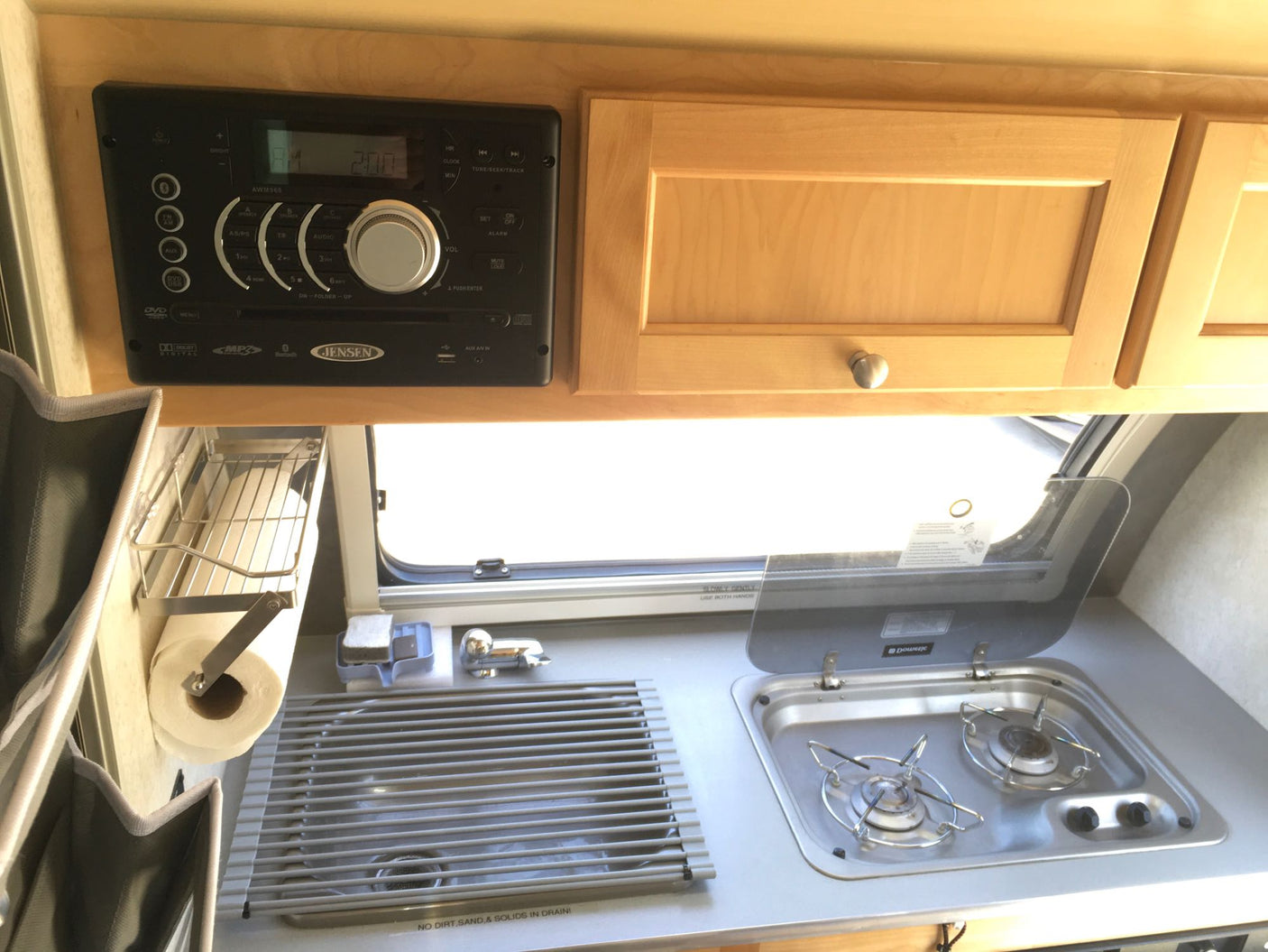 Compact rv rental galley featuring a Jensen stereo, sink, and two-burner stove setup.
