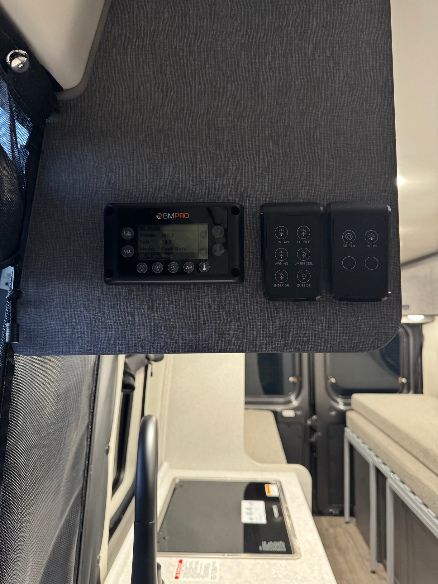 Inside an RV rental: overhead control panels for lights and temperature, with a compact kitchenette and bed area visible.