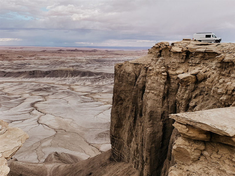  parked among striking desert rock formations.|A white RV rental is parked on a dramatic desert cliff overlooking a vast — photo 2