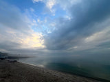 Cloudy morning at a calm beach, perfect for unwinding after an RV rental journey. Gentle waves, hazy distant shore.