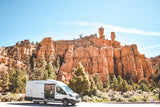 RV rental van at scenic red rock canyon under blue sky with trees. Ideal for adventure & van life.