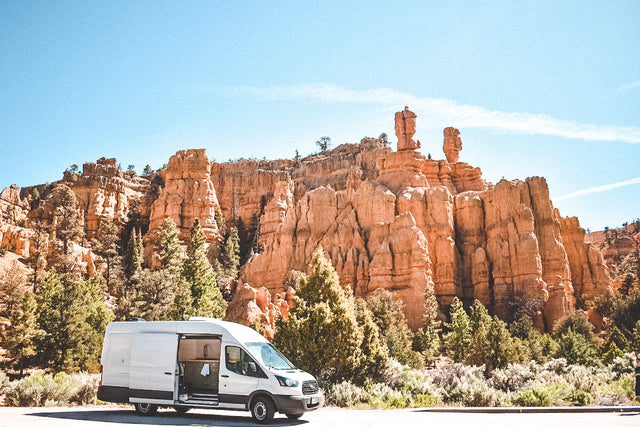 RV rental van at scenic red rock canyon under blue sky with trees. Ideal for adventure & van life.