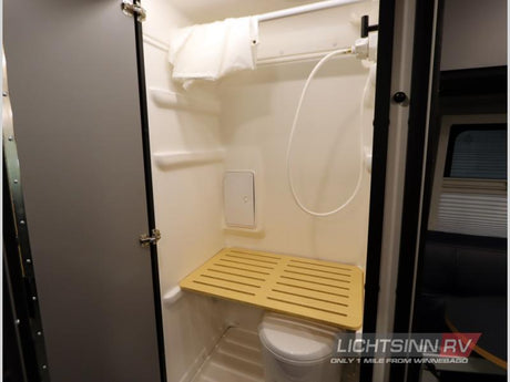 Inside this RV rental, find a compact shower with a hose, small toilet, and a slatted wooden seat for comfort.