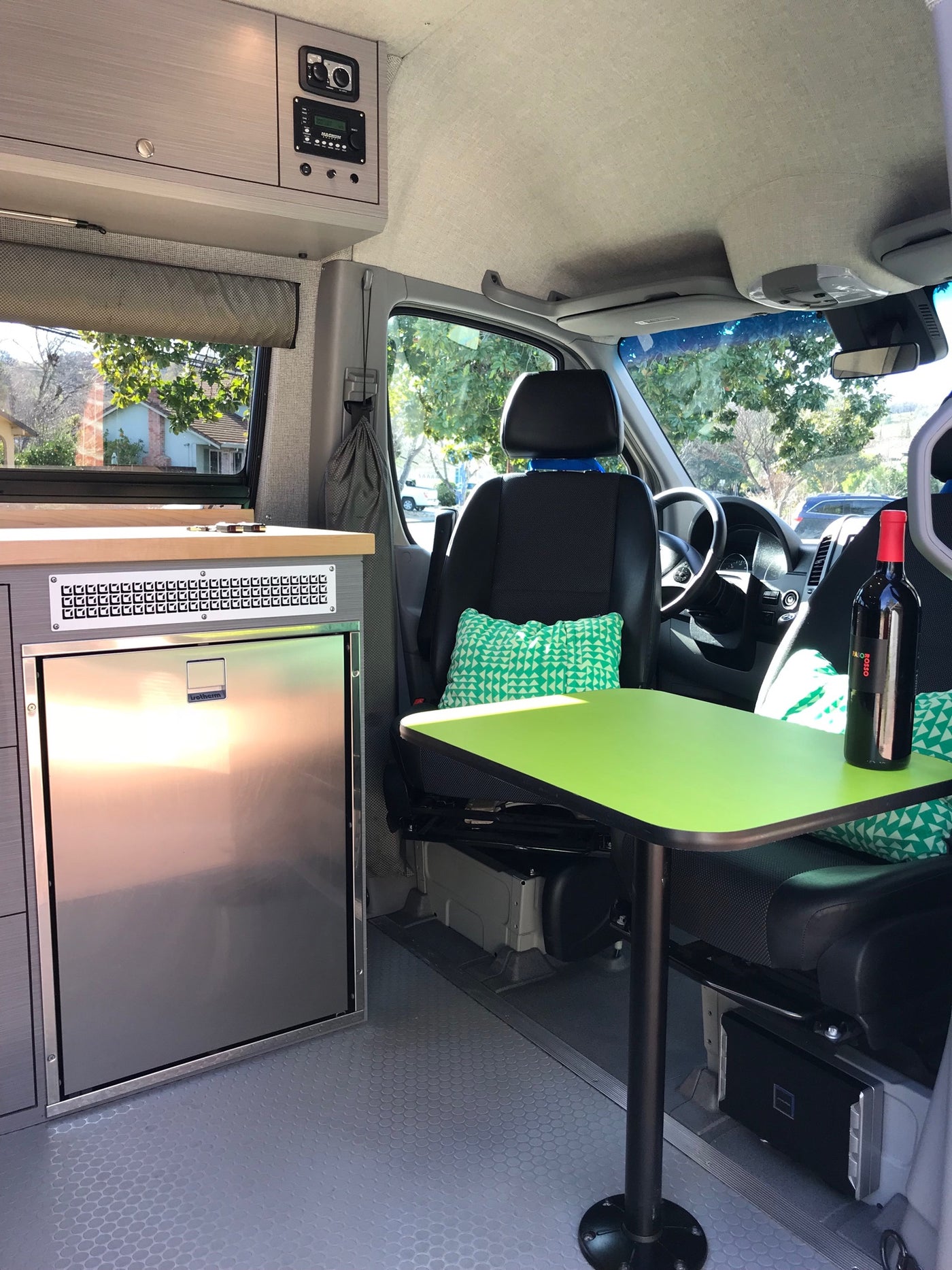 Modern RV rental conversion: comfy swiveling seats, bright green table, kitchenette with fridge & controls. Perfect for travel. — photo 8