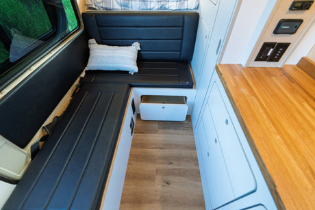 RV rental: Spacious camper van interior with black bench seating, storage, wood floor, and sleek countertop.