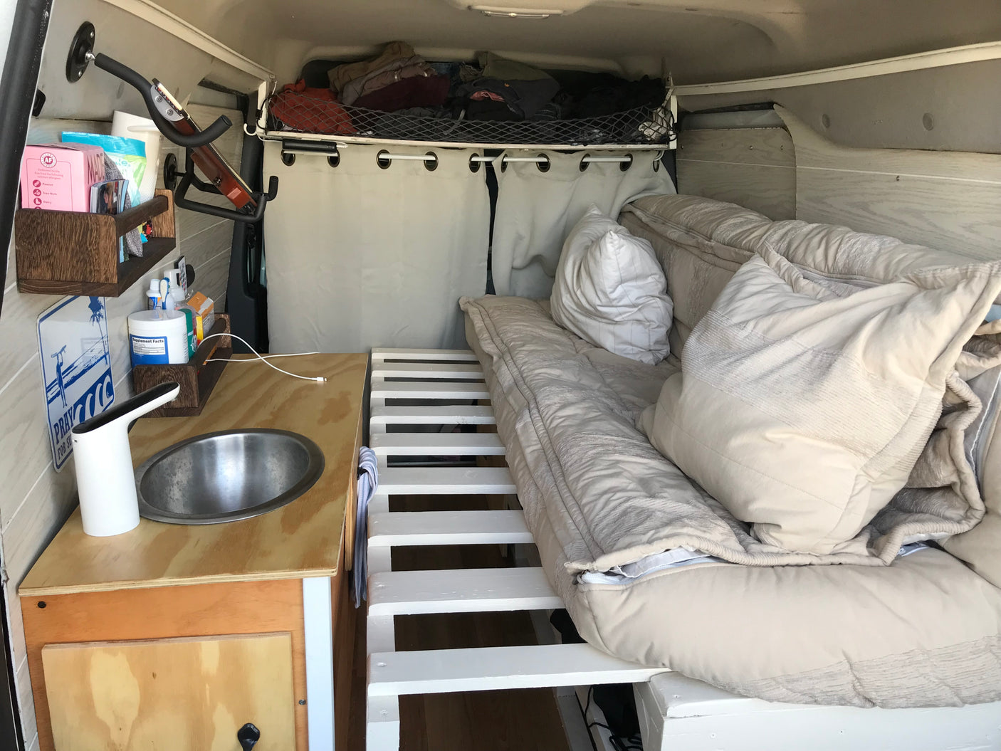 Cozy RV rental interior with a comfortable bed, kitchenette with sink, and overhead storage, perfect for mobile living.