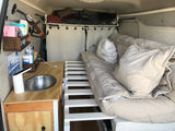 Cozy RV rental interior with a comfortable bed, kitchenette with sink, and overhead storage, perfect for mobile living.