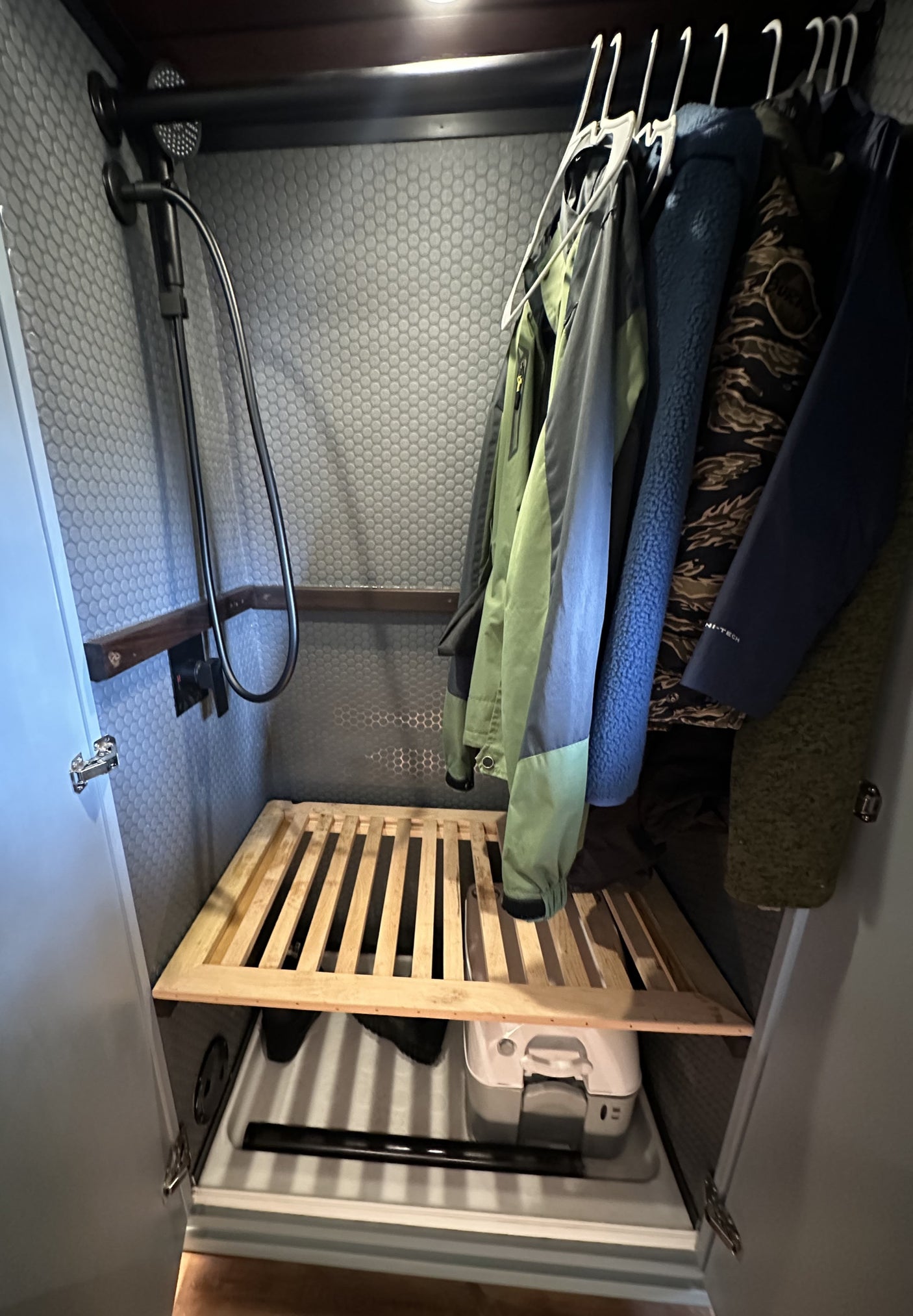 RV rental: Compact shower/closet with hanging clothes, wooden slatted shelf, and portable toilet.
