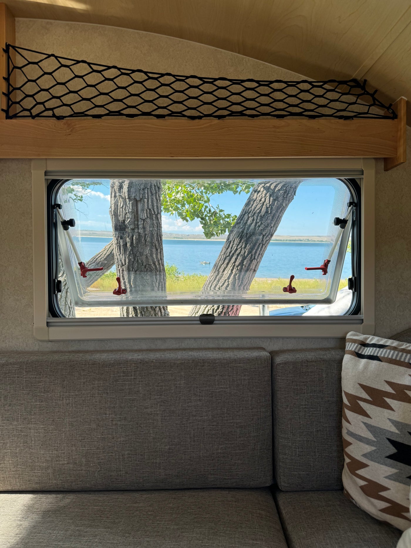Cozy RV rental interior with an open window revealing a serene lake view between tree trunks, perfect for nature getaways. — photo 20