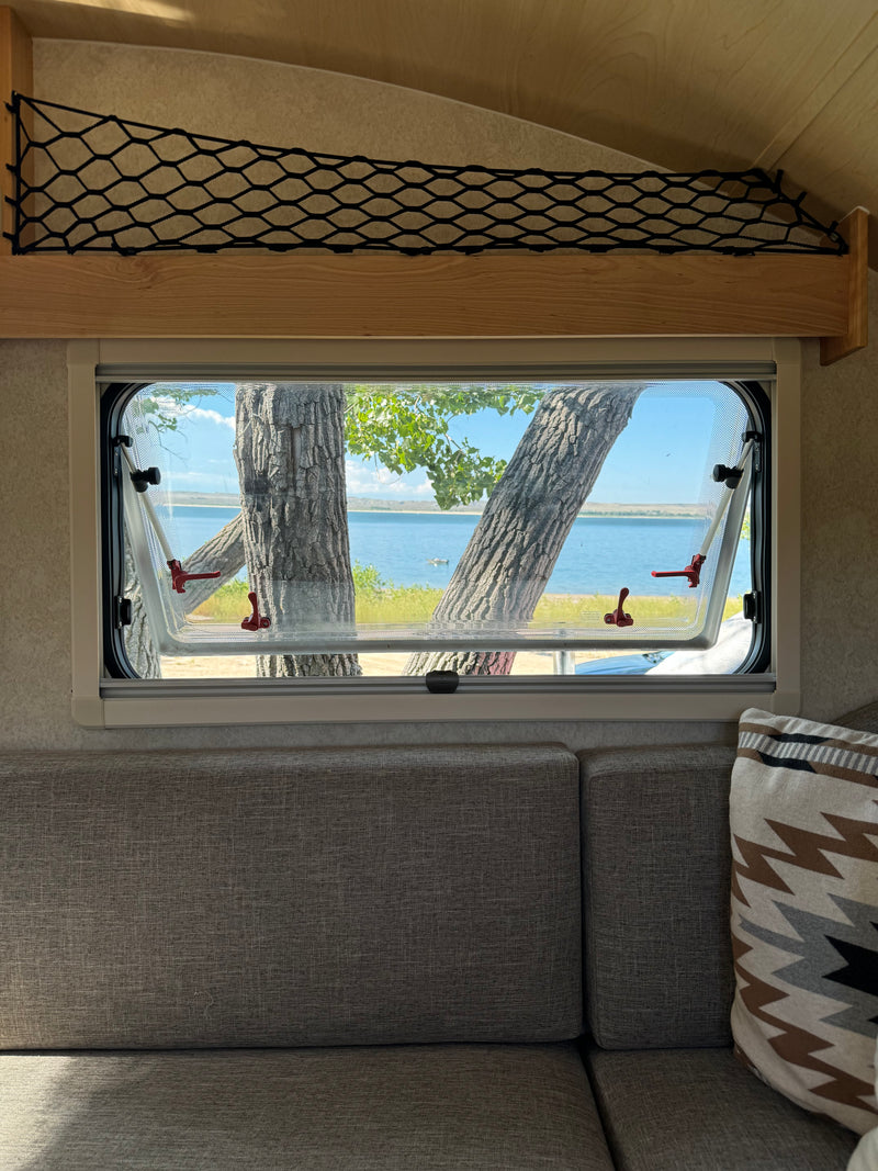 Cozy RV rental interior with an open window revealing a serene lake view between tree trunks, perfect for nature getaways. — photo 20