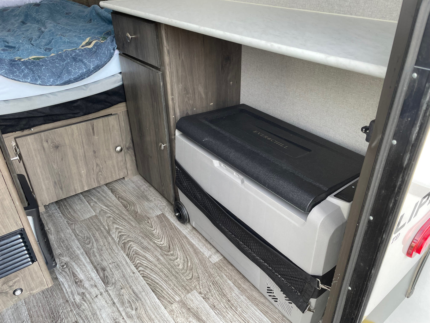 Inside an RV rental: a bed, wood storage cabinets, and a portable Everchill refrigerator with wheels.