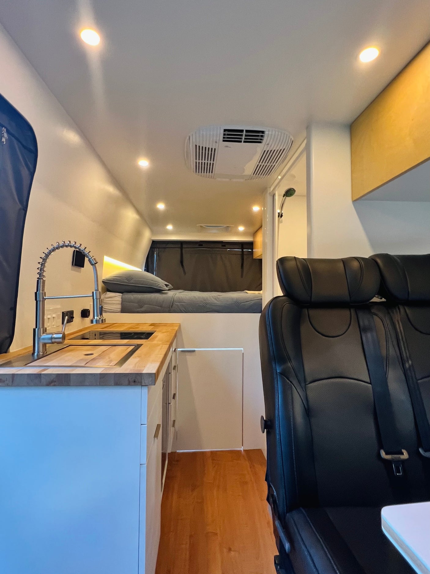 Modern rv rental interior featuring a functional kitchen, cozy bed, and front seats, creating a compact and well-lit living space.