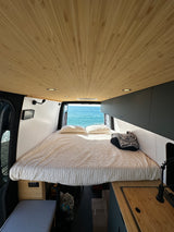 Enjoy this RV rental's cozy interior, featuring a wood-paneled ceiling, comfy bed, and stunning ocean view.