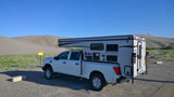 White pickup with Palomino truck camper, a versatile RV rental, parked by desert sand dunes.
