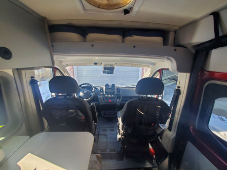 Inside an RV rental, a view from the living area towards the front cockpit with driver & passenger seats and overhead storage.
