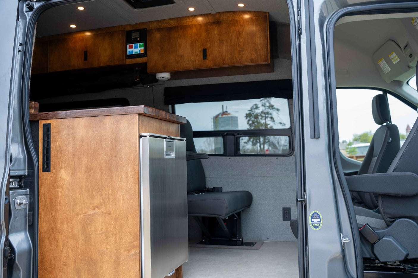 Spacious RV rental interior featuring wooden cabinets, a stainless steel fridge, and comfortable seating with a scenic view.