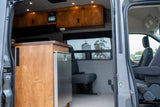 Spacious RV rental interior featuring wooden cabinets, a stainless steel fridge, and comfortable seating with a scenic view.
