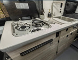  flowery forest clearing with a person relaxing.|This RV rental's compact kitchen features a two-burner stovetop