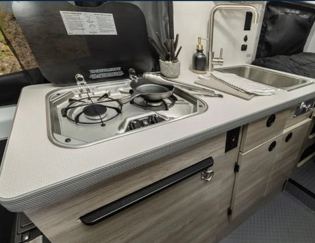  flowery forest clearing with a person relaxing.|This RV rental's compact kitchen features a two-burner stovetop
