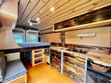 Beautiful custom wood camper van interior, ideal for your next RV rental adventure. Features a kitchen, bed, and seating.