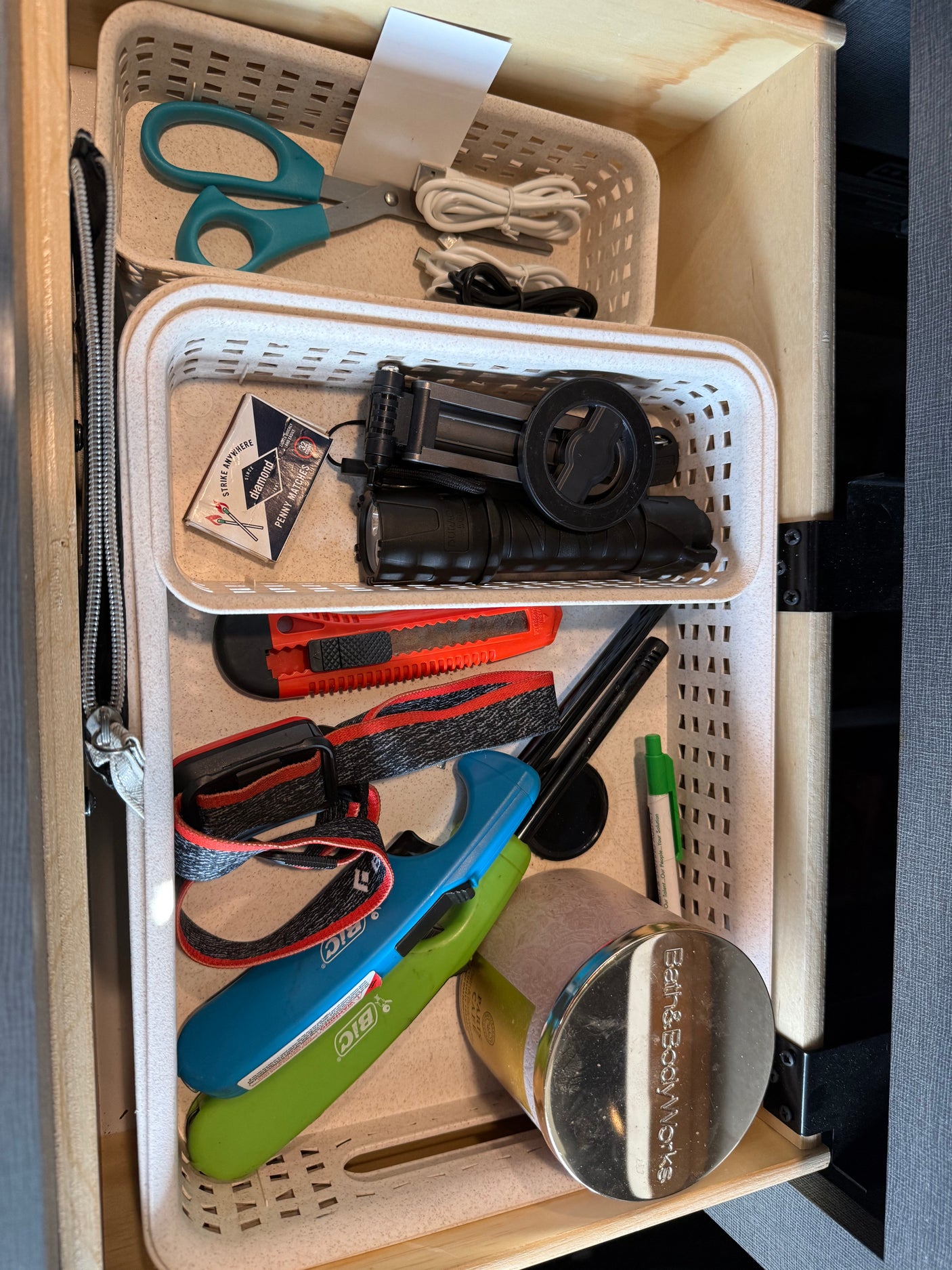 RV rental drawer: Organized essentials include scissors, USB cables, matches, flashlight, utility knife, headlamp, lighters, pen, and a candle.