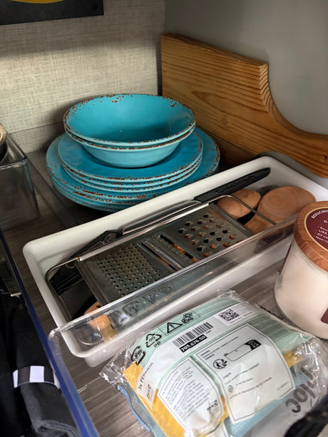 An organized rv rental kitchen with blue dishes, a Cuisinart grater, wooden utensils, and IKEA cloths, neatly stored.