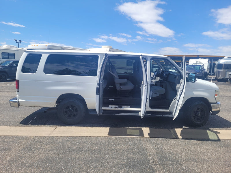 White passenger van with all side doors open, parked at an RV rental facility among other RVs under a blue sky. — photo 7