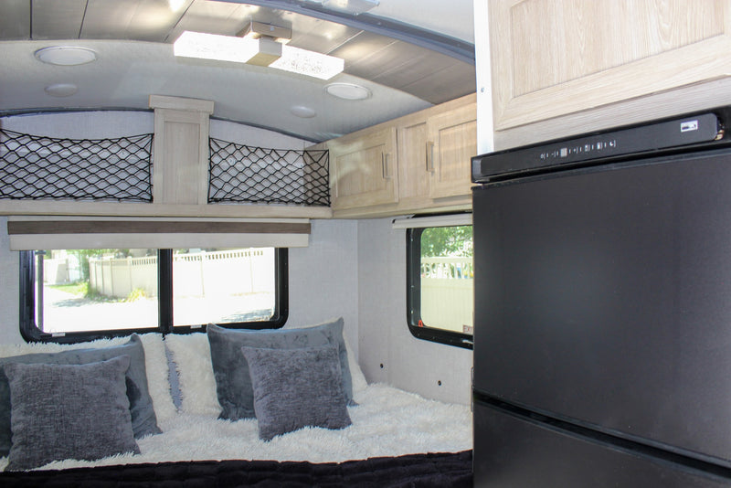 Modern RV rental interior featuring a bed with plush pillows, overhead cabinets, and a compact fridge. — photo 14