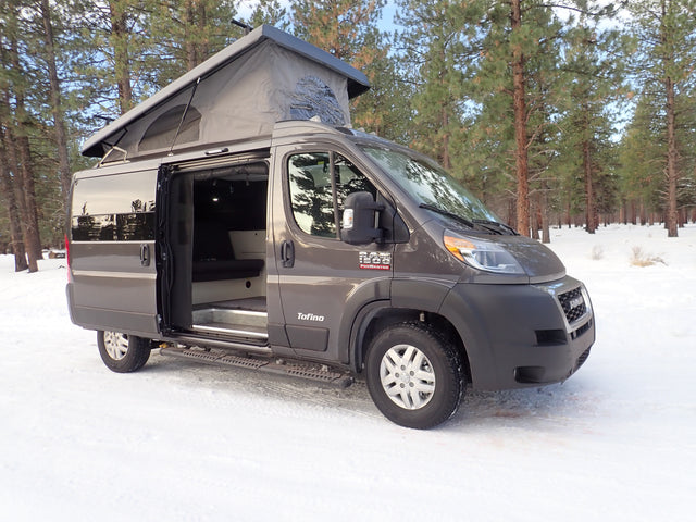 Gray pop-top camper van for your next **rv rental** winter adventure, parked in a serene snowy forest. Side door open.