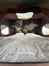 Comfortable bed in an RV rental, featuring a unique world map headboard and bright window views.