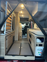 RV rental interior: A spacious van conversion with a convertible bed, storage, and water utility panel leading to the cockpit.