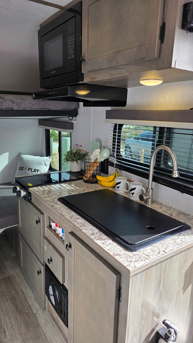 Modern RV rental galley featuring a microwave, cooktop, sink, and countertop space with kitchen essentials. — photo 19