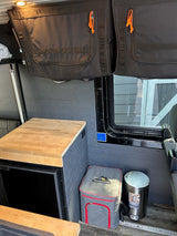 This RV rental interior features practical overhead storage, a mini-fridge with counter, cooler, and trash bin.