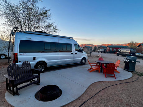 Silver Boldt campervan RV rental setup at a scenic campsite, complete with a patio, fire pit, and BBQ grill.