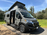 A gray Winnebago Solis pop-top camper van, ready for RV rental adventures with its side door open, parked outdoors.