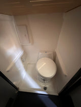 Inside this RV rental, a compact, bright white wet bath features a toilet and an integrated shower drain on the floor.